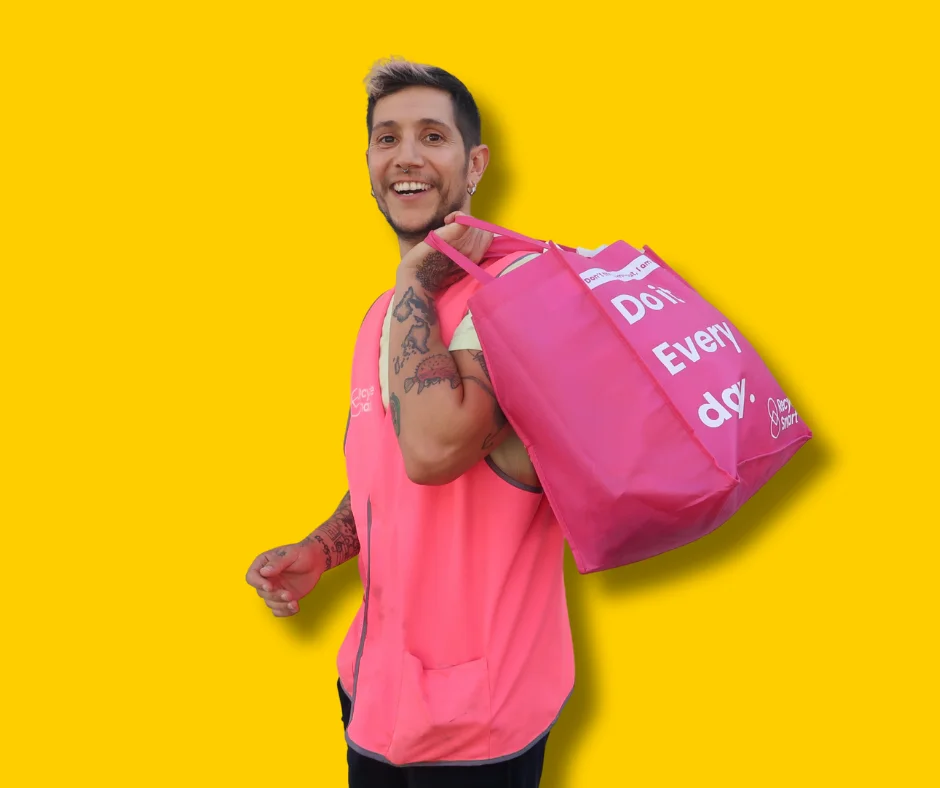 Smiling ReSmart driver in a pink vest carrying a pink ReSmart bag, on a yellow backdrop