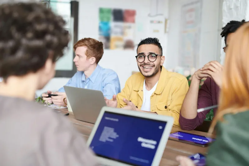 Colleagues smiling around laptops at a meeting table